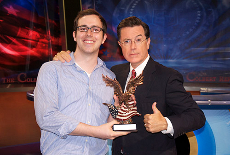 Developer holding an award next to Stephen Colbert